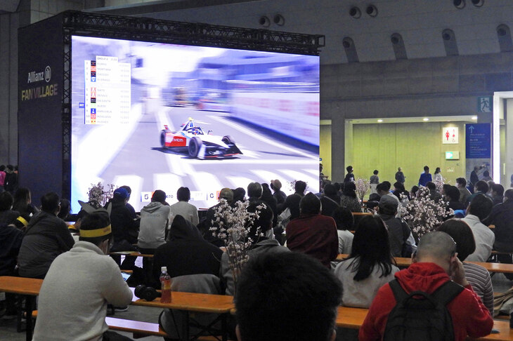 そうこうしているうちに、フォーミュラEの予選がスタート。予選ではまずドライバーをA、Bの2グループに分けてタイムアタックを行い、各グループの上位4名（全8名）がクオーターファイナルに進出。その後はトーナメント方式、すなわち“一対一”でタイムアタックを行い、勝ち残った1名がポールポジションにつくこととなる。写真はファンビレッジにて、スクリーン越しに予選を見守る来場者の様子。