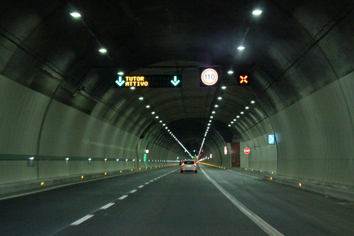 バイパスのトンネルは明るく、非常用の路側帯もある。頭上の電光表示は、区間平均速度計測式自動速度取り締まり機「チューター」作動中を示す。