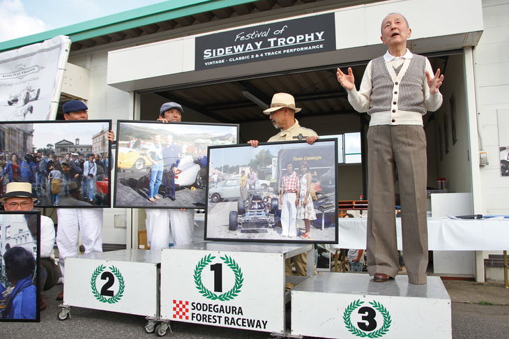 全レース終了後、表彰式にて入賞者にカップを授与。その後に締めのプログラムとして、恒例となった生沢さんのトークが行われた。今回のお題は、彼がヒストリックイベントについて思うところ。大きく引き伸ばした写真パネルを何枚も用意するなどして貴重な話を聞かせてくれたが、彼のファッションにも注目。まるで1970年代前半のメンズファッション誌『男子専科』から抜け出てきたようなコンチネンタル（ヨーロピアン）スタイルの千鳥格子のニット、バギーパンツにハイヒールシューズという今回のアイテムは、すべて当時モノ。知る人ぞ知る物持ちの良さもさることながら、それらがそのまま着られる、つまり体形が変わっていないこともあっぱれというほかない。