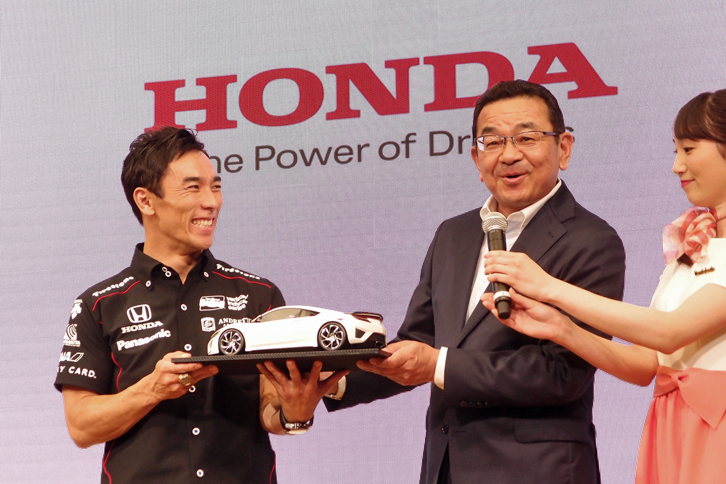 報告会では、本田技研工業の八郷隆弘代表取締役社長（写真右）も姿を見せ、佐藤の勝利を祝福。記念の品として、スーパースポーツ「NSX」を贈呈した。「これはミニチュアですが、ちゃんと実物を差し上げます」という社長のコメントに、佐藤も大笑い。
