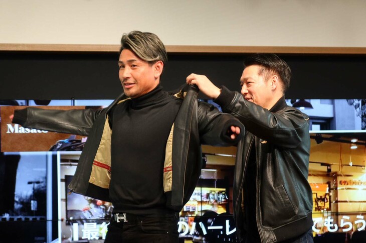 ハーレーダビッドソン ジャパンの野田一夫 代表取締役（写真右）から魔裟斗さんに、ハーレーダビッドソンのレザージャケットのプレゼント。袖を通した魔裟斗さんは「柔らかい着心地で、バイクの運転がしやすそうですね」と満足の様子。