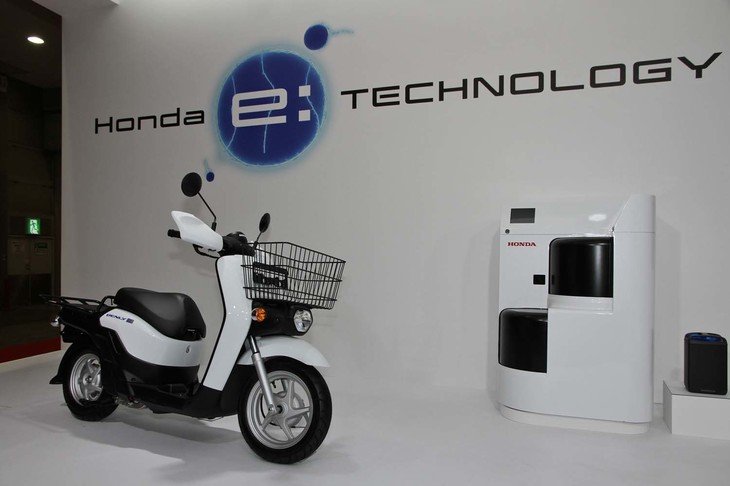 ワンタッチで交換できるバッテリーを2個搭載した「ベンリィe:」。右は街中に設置される充電スタンド。6個のバッテリーを収納・充電できる。