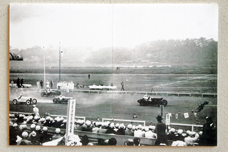 写真の中で筆者が気になった1枚。手前の看板には「日産自動車指定席」とあり、その下にはダットサンの旗とおぼしきものが。今日のSUPER GTで見られるNISMO応援団のルーツか？