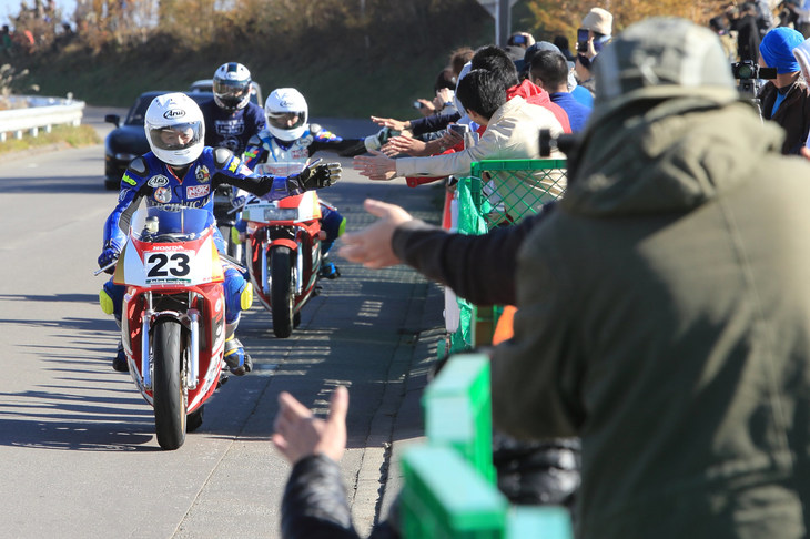 観客とハイタッチしながら観覧エリアを通過する「ホンダNSR250R」（手前）と「NSR250R SP」（奥）。言わずと知れた2ストローク時代の名車である。