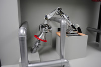 原発事故現場での活躍が期待される作業アームロボット。赤い部分がバルブの操作部。ここに銀色のジグをはめ込み、先端を回転させることでバルブを開閉する。バルブ手前のパイプを避けて作業を行っている点に注目。この写真はデモ用にカバーを取り去ったもの。