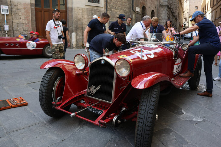 1931年「アルファ・ロメオ6C1750GSスパイダー ザガート」が応急修理を受ける様子を人々が見守る。