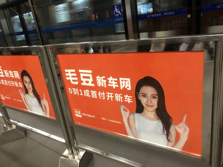 モーターショー期間中は、お買い得車検索サイトの広告も駅構内に花盛り。これはそのひとつである毛豆（マオドウ）。イメージキャラクターは香港モデルのアンジェラベイビーである。