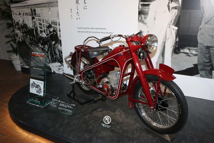 ホンダ初の本格二輪車「ドリームD型」。当時一般的だった鋼管フレームではなく、量産性を考慮したプレス鋼板のチャンネルフレームを採用。黒いバイクがほとんどという中、美しいマルーン色の車体も注目された。チェンジペダルのみで変速可能な2段トランスミッションを搭載し、この機構が、のちに「スーパーカブ」に採用される自動遠心クラッチへとつながった。