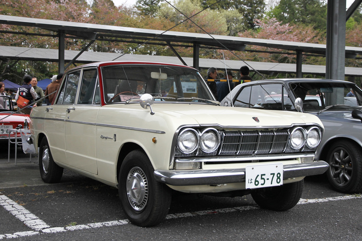1966年「プリンス・スカイライン2000GT-A」。型式名S54A-2こと初代スカGの、シングルキャブ仕様の2リッター直6 SOHCエンジンを積んだおとなしいほうのモデル。アイボリーに赤いトップのツートンカラー、キャップ付きの純正スチールホイールにハイトの高いタイヤという、カタログから抜け出てきたような姿で、程度もすばらしい。