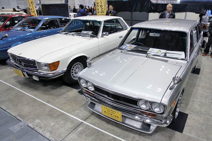 エンジンをオリジナルのL14からソレックスキャブなどでチューンされたL16（1.6リッター）に積み替え、5ナンバーのワゴンとして公認済みの1971年「ダットサン・ブルーバード1400バン デラックス」（右）と、フルオリジナルのディーラー車という1974年「メルセデス・ベンツ450SLC」（左）。価格は2台とも324万円。新車価格（510バン＝60万円前後、450SLC＝850万円）を知る身としては驚き以外の何物でもないが、これが現在の市場価格なのだろう。ちなみに1984年「カローラ レビン3ドア1600GTV」（AE86）も同じ324万円だった。オートサークルのブースにて。