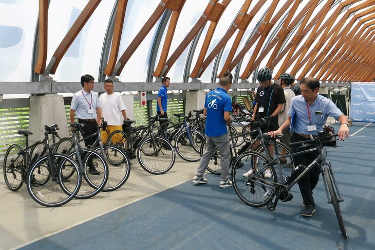 会場に並べられた「RAIL ACTIVE-e（レイルアクティブイー）」と、試乗の準備を進める報道関係者およびワイ・インターナショナルのスタッフ。