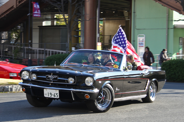 アメリカ国旗をなびかせながらロータリーを回る1965年「フォード・マスタング コンバーチブル」。