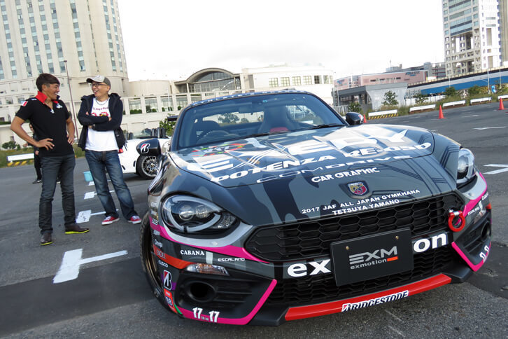 全日本ジムカーナ選手権において、「PN-IIクラス」でシリーズ優勝を果たした、山野哲也選手（左）の「アバルト124スパイダー」。イベントの司会進行を務めたDJのピストン西沢氏（右）も、このクルマに興味津々（しんしん）の様子だった。