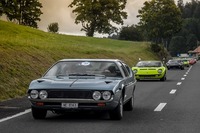 スイスののどかな景色を背景に、カラフルなスーパーカーの一群が行く。