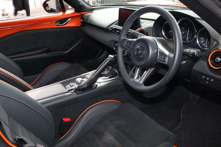 オレンジのアクセントが際立つインテリア。ドアトリムやインストゥルメントパネルなどには、アルカンターラが用いられている。仕様自体はソフトトップの記念車と同じだ。オーディオは、BOSEサウンドシステム＋9スピーカー仕様。