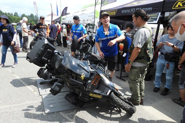 誰かがバイクを倒しちゃったか!?　……と思ったが、さにあらず。こちらはアメリカ発のアパレルブランド、Klim（クライム）のブースで、バイクが倒れてもつぶれないサイドバッグの実演をしていたのだ。