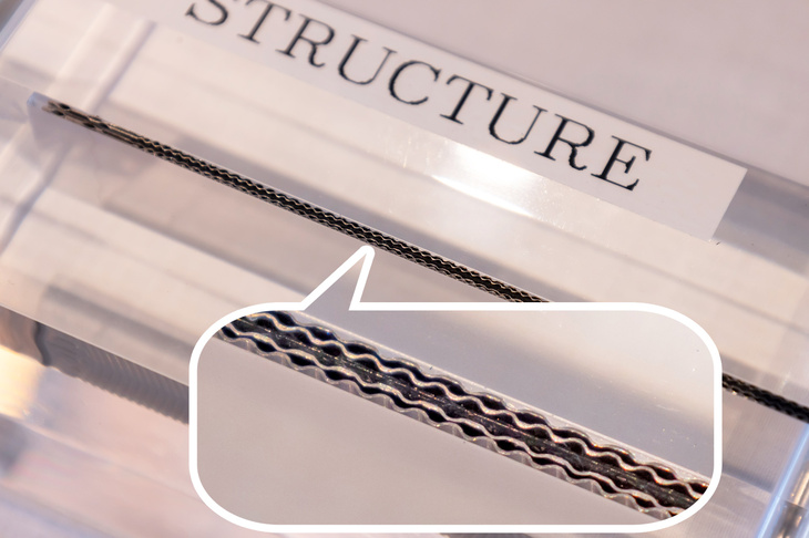 FCセルの断面図。中央の黒い帯が電極集合体で、その上下を2枚の金属プレートからなるセパレーターが挟んでいる。電極集合体とセパレーターのすき間を水素／空気が、セパレーター内の空洞を冷却水が通る。