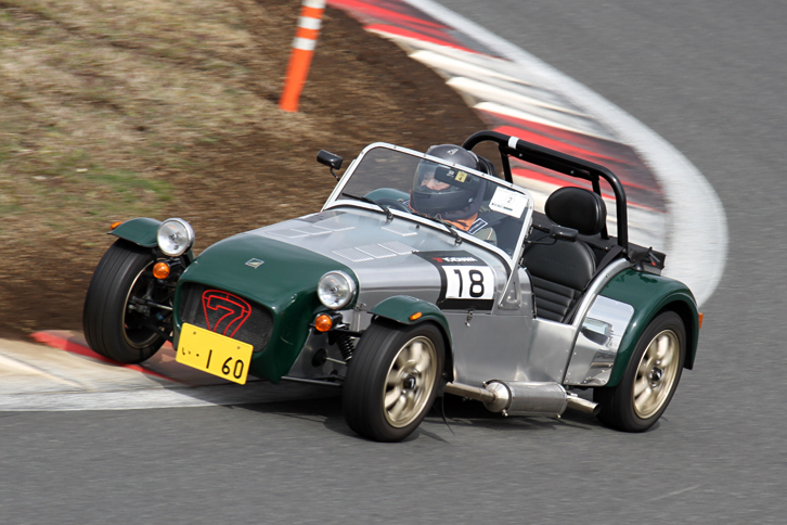 縁石を大きく使って1コーナーを行く、黄色ナンバーの付いた「ケータハム・セブン160」。