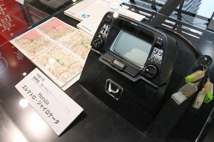 1981年に「ホンダ・アコード／ビガー」にオプション設定された「エレクトロ・ジャイロケータ」。車両に搭載したジャイロセンサーで進行方向、車速センサーで走行距離を検出する自立航法による世界初のカーナビ。CRTディスプレイに透明フィルムに印刷された地図をセットし、現在位置を確認しながら予定したルートをトレースしていくもので、ルート案内はしてくれない。長距離の場合は、左側に置かれたファイルに収められた地図の差し替えが必要だった。