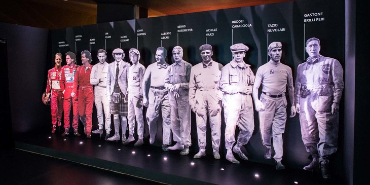 「フォームラ」のスペースに置かれた歴代ドライバーの姿。右端は1903年生まれの、自転車／二輪／四輪のレーサー、ガストーネ・ブリッリ・ペーリ。四輪でのデビューは1920年。一番左はミハエル・シューマッハー。F1で7度チャンピオンに輝いた。並んでいる12人はタツィオ・ヌヴォラーリ、ジョン・サーティース、ジャッキー・スチュワート、ジム・クラーク、アイルトン・セナなど、いずれも伝説を生み出したドライバーたち。