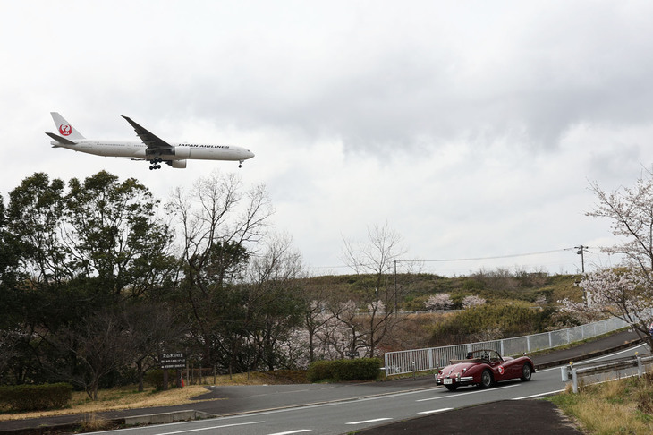 ゴールに向かう1955年「ジャガーXK140 DHC」と成田空港への着陸直前の日航機のツーショット。
