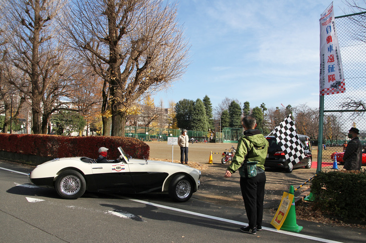 谷保第三公園の入り口でチェッカードフラッグが振られ、ゴールインする通称“ビッグヒーレー”こと「オースチン・ヒーレー100」。