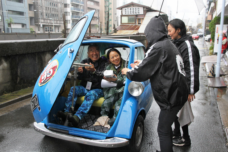 PC競技を終え、女性スタッフからおみやげの和菓子を受け取る1961年「BMWイセッタ300」に乗るペア。ちなみに和菓子はスタッフの後方、路地に面している梅花亭謹製。