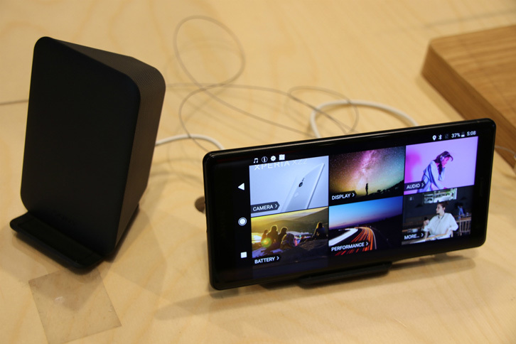 こちらは、ソニーの最新スマートフォン「Xperia XZ2」（写真右）。映像の音声に連動して本体が振動する。専用のワイヤレス充電クレードル（左）は縦横いずれの向きでも使用可能。