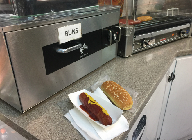 クルマの到着を待つ間、ガソリンスタンドでホットドッグを食す。バンズ（パン）は、客が自分で容器から取り出してソーセージと合体させる。