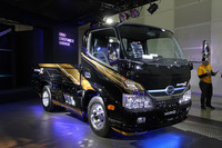 紫がかった照明もあやしげな「日野」のブースに展示された「デュトロ ハイブリッドカーゴ」。ちなみに隣のブースは、毎回露出度の高いコスチュームで話題となる「AIWA」とあって、おそらくハンパでない数のカメコ（カメラ小僧）を集めるエリアとなるはず。