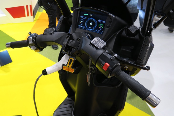 aideaの電動三輪スクーターのバッテリーは非脱着式で、コードでつないで充電するタイプ。CHAdeMOに対応しているものもあるという。特徴は、給電機能が付いていて、車載バッテリーの電気を家やオフィスで使えるところ。若いスタッフは「配送用スクーターとしては価格は高いですが、設置型バッテリー＋スクーターとして考えていただけたら、競争力はあるはずです」と勇ましい。