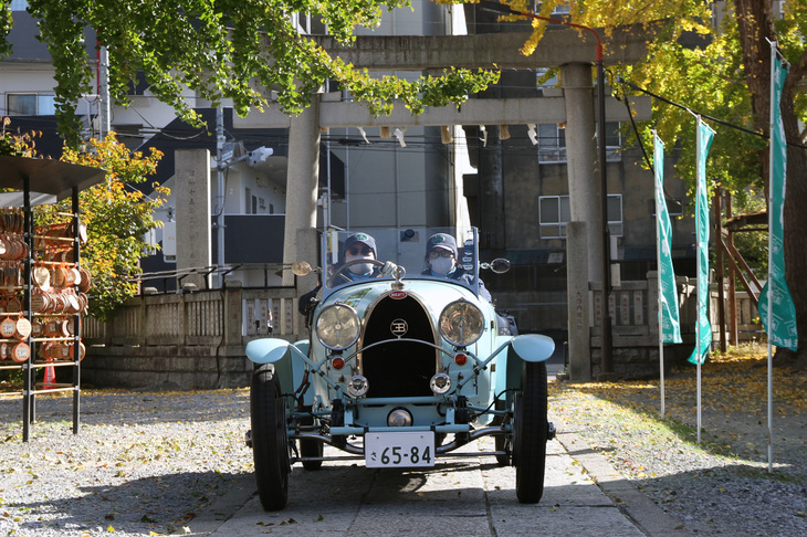 チェックポイントである浅草・今戸神社の鳥居をくぐり、境内を行く1928年「ブガッティT40」。ドライバー／コドライバーは、ラ フェスタ ミッレミリア8連覇をはじめ国内のクラシックラリーで幾多の勝利を挙げている最強ペアの竹元夫妻。