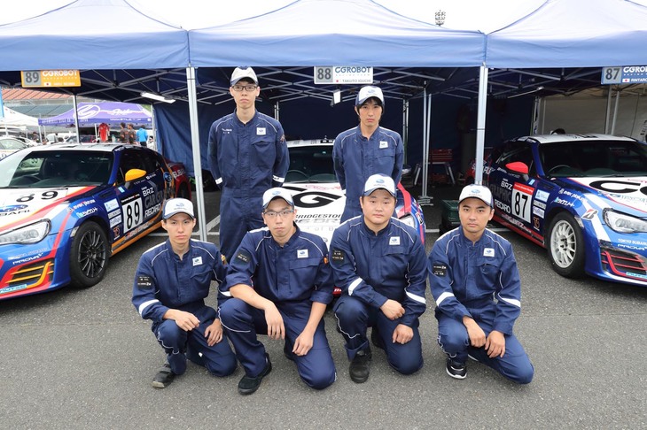 今回のもてぎラウンドでCG ROBOT RACING TEAMに心強い助っ人として加わってくださったスバル・ディーラー・メカニックの皆さん。前列左から橘 和弘メカ（福島スバル自動車 郡山店）、飯田恭史メカ（東京スバル 小松川店）、崔 允煥メカ（東京スバル 多摩店）、吉原邦康メカ（富士スバル 伊勢崎つなとり店）、後列左から、太田 実メカ（千葉スバル自動車 浦安店）、清水祥太メカ（栃木スバル自動車 佐野店）の6人である。