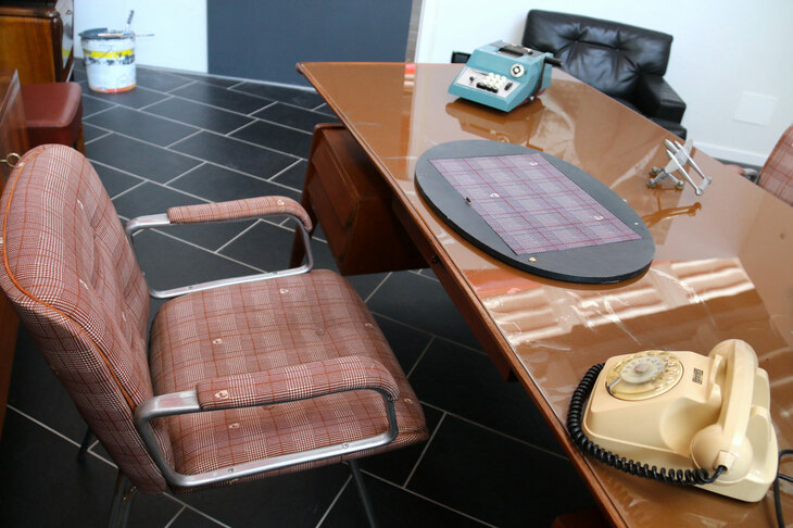 椅子に張られたチェックの生地には、ファイティング・ブルのマークが。机上には伝説のオリベッティ製機械式計算機「スンマ・プリマ20」がある。