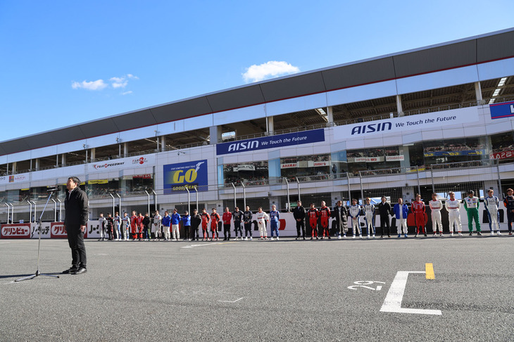 正午過ぎに行われたウエルカムセレモニー。出場全ドライバーと監督、そしてレジェンドドライバーがメインストレートに整列し、日産モータースポーツ＆カスタマイズ株式会社の専務執行役員にしてSUPER GT GT500クラスの総監督を務める木賀新一氏があいさつ。