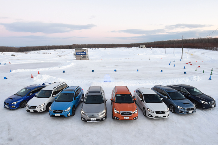 雪景色の新千歳モーターランドにずらりと並んだ、試乗用のスバル車。写真左から、「WRX STI」「エクシーガ クロスオーバー7」「XV」「レガシィアウトバック」「フォレスター」「インプレッサスポーツ」「レヴォーグ」「レガシィB4」。水平対向4気筒エンジンを搭載する4WD車である点は全車共通だが、採用されている4WDシステムのタイプは、4つ（アクティブトルクスプリットAWD／不等＆可変トルク配分電子制御のVTD方式AWD／ドライバーズコントロールセンターデフ付きのDCCD方式AWD／ビスカスLSD付きセンターデフ方式AWD）に大別される。