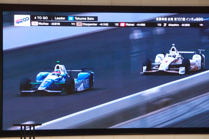 会場で放映された、今回のインディ500を振り返る映像から。レース終盤、首位に立った佐藤（写真左）が、優勝に向かってラストスパートをかける。