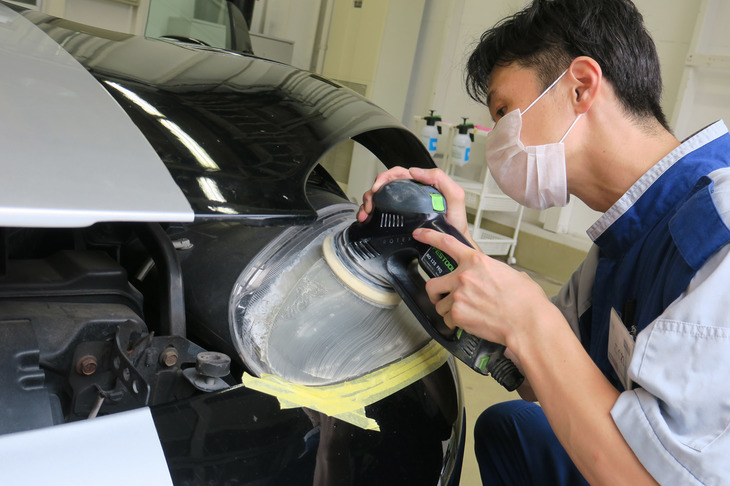 ヘッドランプのレンズをクリーニングする小暮氏。塗装が傷んでいたので、研磨に際してはマスキングテープを貼る／剥がす作業も慎重に行われた。