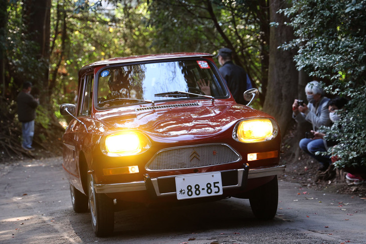 近乗会（パレード）に出発すべく、本殿から参道入り口に続く坂道を駆け登る車両。往年のフランス車（フランス仕様）ならではのイエローバルブの異形ヘッドライトをともして行くのは1970年「シトロエン・アミ8ブレーク」。