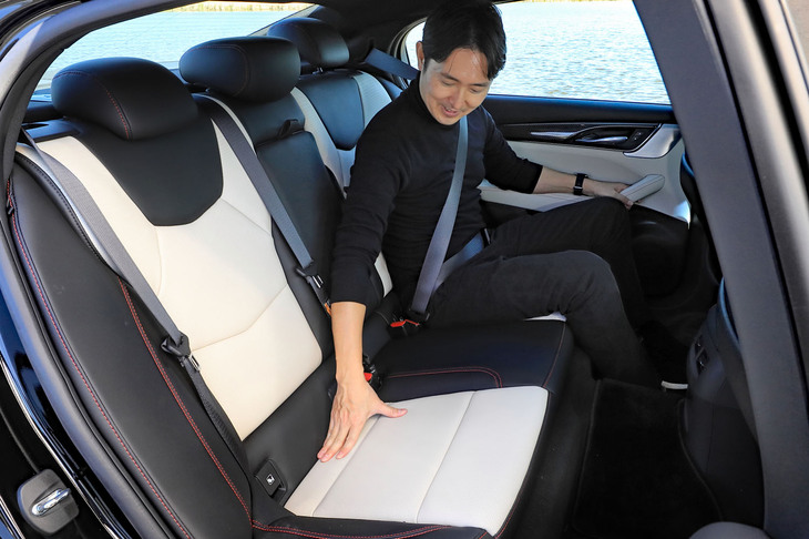 後席の座り心地をチェックするアレック氏。空間効率では不利なFRベースのセダンでありながら、足もとスペースは広々としている。