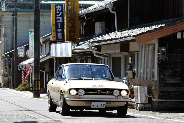いわゆるハンドメイド時代の1970年「いすゞ117クーペ」。ちなみにカンコー学生服の看板のある洋品店、土曜に下見で通過した際は営業中で制服が飾られていた。