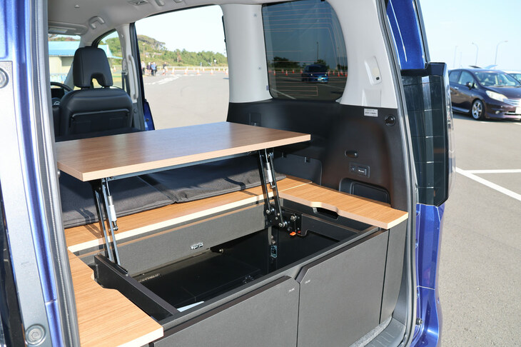 こちらの車中泊車の秘密は、最後部に引き上げタイプのデスクが備わること。デスクを起こすと、掘りコタツのように足を下ろせるので、作業や休憩もしやすくなるというわけだ。さらに床下は、収納としても使える仕組みとなっている。