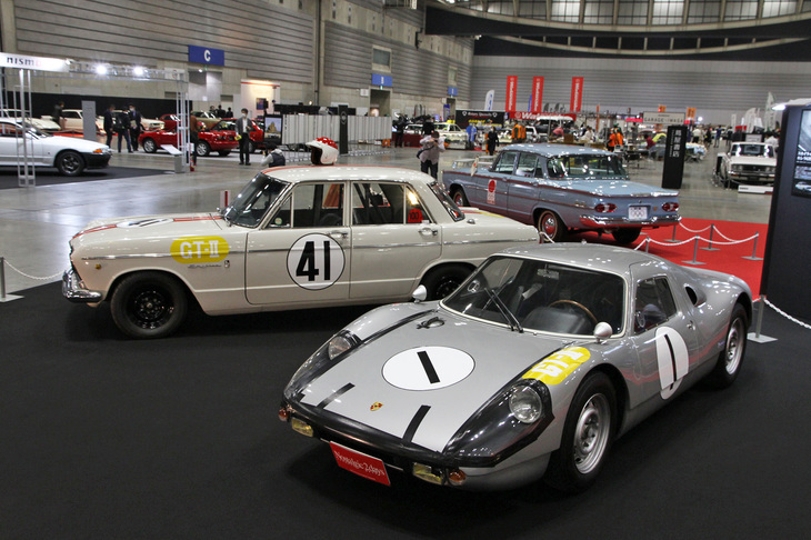 今回の企画展のテーマは「1964年にちなんだ車両」。これら2台は、1964年の第2回日本グランプリに向けて必勝を期してつくられたGT-IIクラス用のホモロゲーションモデルである「プリンス・スカイラインGT」（レプリカ）と、レース直前に急きょ空輸されスカイラインGTに立ちはだかった、最新鋭のミドシップスポーツである「ポルシェ・カレラGTS」（904）。本来なら勝ち目はまったくない、ファミリーセダンがベースのスカイラインGTが、練習走行中のクラッシュによって完調には遠かったポルシェを決勝で一瞬ながらリードした……というスカイライン伝説誕生の歴史的瞬間を再現している。