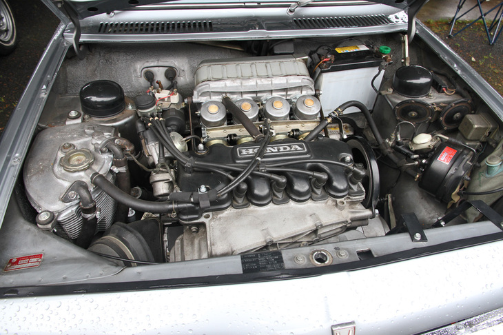 「ホンダ1300 99S」のエンジンルーム。4連キャブレターを備えた99では、さらにパワーアップされ最高出力115ps/7500rpm、最大トルク12.05kgm/5500rpmを発生。空冷エンジンではオイルによる冷却も重要であることから、H1300ではレーシングマシン譲りのドライサンプを採用。左端にあるオイルタンクもエンジン同様アルミ製で、冷却フィンが切られている。DDACは水まわりのメンテナンスが不要でタフという空冷の美点はそのままに、エンジンが二重壁を持つゆえ、泣き所である騒音は水冷並みに抑えられた、とホンダはうたっていた。反面、複雑な構造ゆえに大きく重くなり、コストも上昇。シンプルで軽量、低コストが特徴の一般的な空冷とは正反対のエンジンになってしまった。