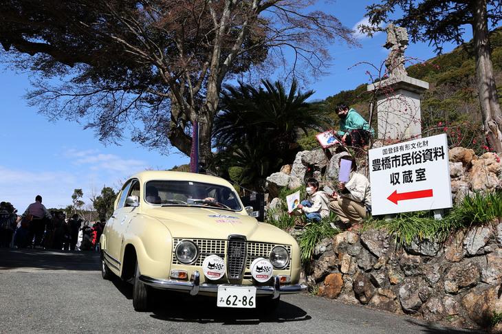 1966年「サーブ96モンテカルロ」。「豊橋市民俗資料収蔵室」という看板の上に、昔の小学校の定番アイテムだった二宮金次郎像が見える。