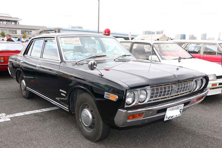 1974年式（昭和49年式）「日産グロリアDX」。あえてスタンダード風仕様にしているとのこと。懐かしの刑事ドラマをほうふつさせる赤色灯がポイント。劇中ではよく大破していた記憶が……。