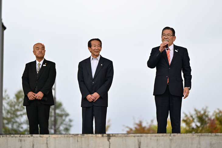 副村長と教育長も従えて登壇した山中湖村の高村正一郎村長（写真右）。10回目となる「山中湖交流プラザ きらら」での開催を喜んでいた。山中湖の隣の明神山にもうすぐ世界一（村長いわく）のパノラマウッドデッキが完成するという。