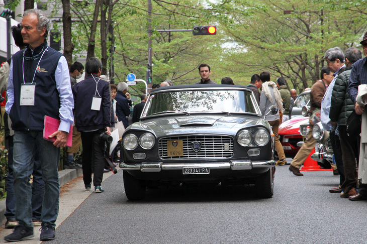 江戸桜通りに最後に到着した、京都からの遠征組の1962年「ランチア・フラミニア コンバーティブル」。イタリアのナンバーの付いた車両の周囲に佇（たたず）む西洋人の姿。一見したところでは、どこだかわからない光景だ。