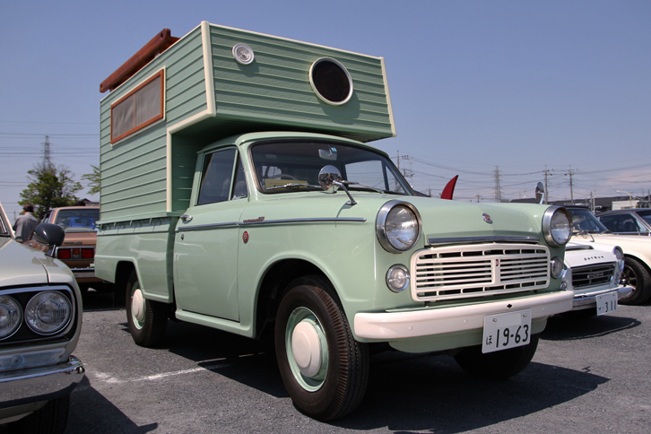 1963年「ダットサン1200トラック」。初代「ブルーバード」の顔を持つダットラだが、荷台には当時風の、しかし新しいキャンパーのシェルが載っている。聞けば、建築士であるオーナーが、現場で余った端材などを利用して自作したものという。