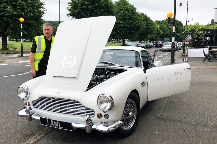 英国のとある交差点にて、立ち往生中の「DB4」と、救援に現れたヘリテージ部門のメカニック。